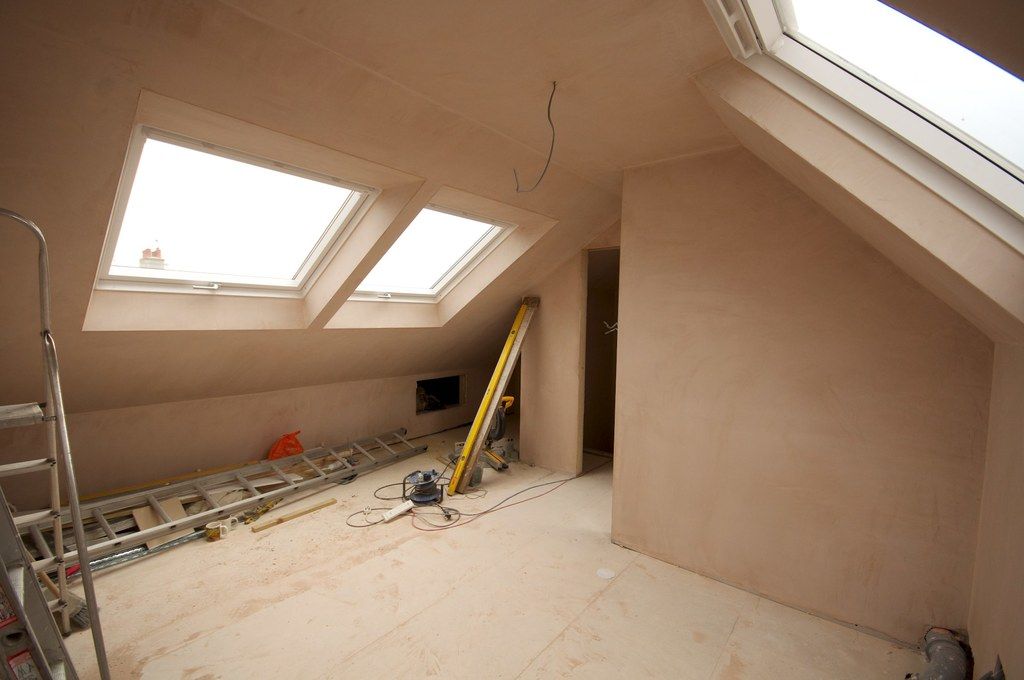 An attic conversion in progress with plastered walls, skylights, a ladder and a spirit level