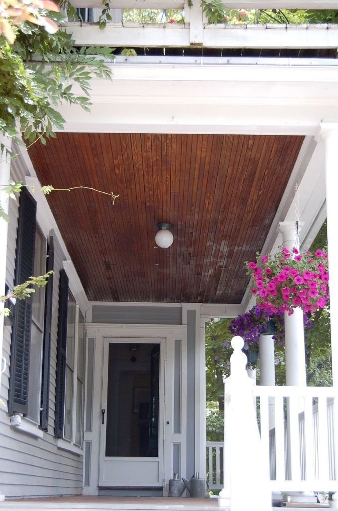 A covered front porch with a stained beadboard ceiling, white railings and hanging flower baskets