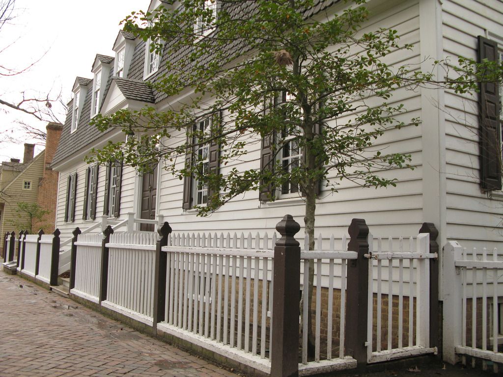 A white clapboard house with dark shutters behind a white picket fence